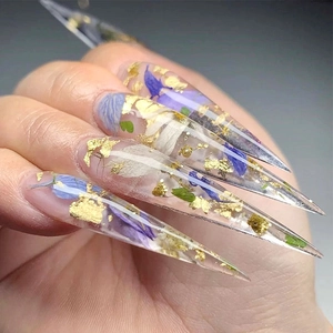Macro detail of transparent nail with purple petals, green leaves and gold leaf flakes