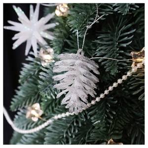 Detail shot of white frosted pine cone ornament with silver glitter on Christmas tree branch