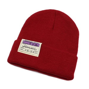 Detailed close-up of dark red knit beanie featuring a vintage boarding pass textile patch