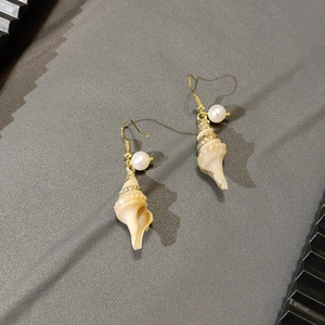 Macro shot of gold conch shell earrings with pearl and shimmering crystal accents