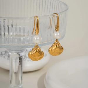 Golden shell earrings with white pearl details hanging on glass for a summer ocean style