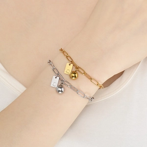 Bracelets à maillons en or et argent avec pendentif lettre Q portés sur le poignet