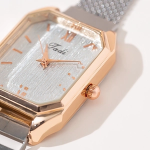 Detailed close-up of rose gold square watch case with silver mesh strap and Roman numerals