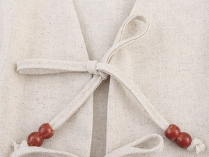 Dettaglio del gilet in lino crema che mostra il laccio laterale e le perline rosse