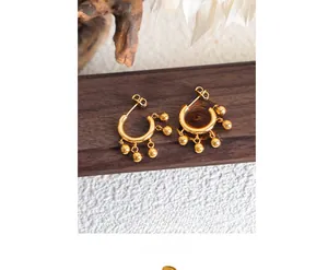 Macro shot of gold C-shaped earrings with five hanging metal spheres on wood