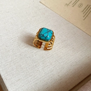 Close-up of 18k gold plated open ring with square turquoise stone on beige fabric