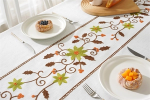 Detail of floral embroidery on linen-textured table runner with festive berries and leaves