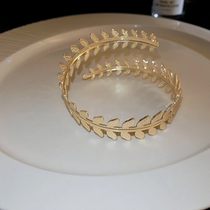 Detailed view of a gold leaf design upper arm cuff on a minimalist white ceramic tray