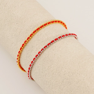 Minimalist red string bracelets with gold and silver beads on a textured pedestal