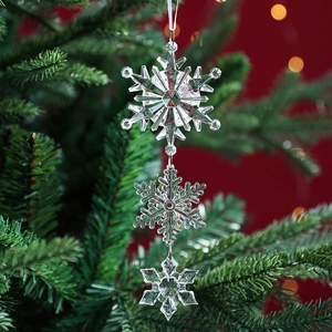 Clear acrylic tiered snowflake ornament hanging on a Christmas tree with festive lights