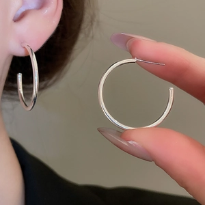 Detail view of silver geometric C-shape earrings shown on model and held in hand