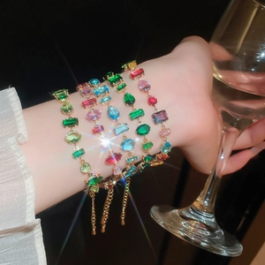 Close-up of five layered gold bracelets featuring colorful geometric zircon stones
