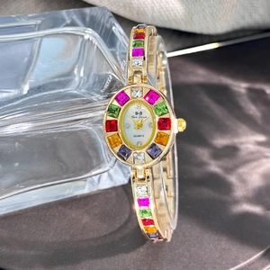 Close-up of golden quartz watch with white dial and colorful gemstone bezel on glass