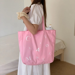 Rosa Canvas-Einkaufstasche mit weißem Buchstabendruck in einem hellen Schlafzimmer-Stil