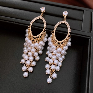Detail of elegant gold tassel earrings with zircon studs and white pearls on black leather