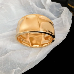 Detail view of wide irregular wave gold metal bracelet with modern textured finish