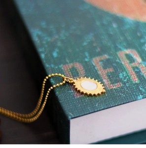 Macro view of gold oval shell pendant with sunburst texture on a stainless steel chain