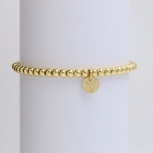 Close-up of a gold-plated beaded bracelet with a polished circular 'Y' letter pendant