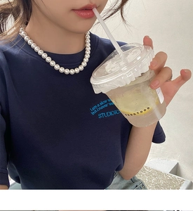 Gros plan d'un collier de perles blanches élégant porté avec un t-shirt bleu marine