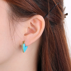 Close-up of heart-shaped blue enamel earring with golden trim worn by a model