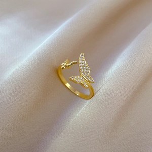 Detailed view of a gold butterfly ring with micro-pave crystals on beige silk fabric