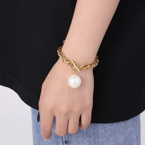 Nahaufnahme eines goldenen Gliederkettenarmbands mit T-Verschluss und weißer Perle