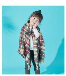 Detail of plaid kids poncho with toggle button and fringe on a soft red fabric
