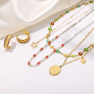Detailed close-up of gold beaded necklaces with colorful floral accents and M-letter pendant
