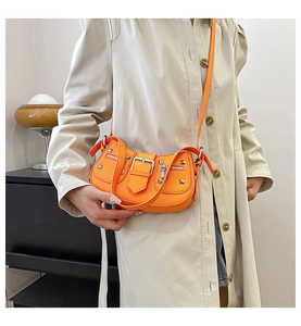 Detail view of bright orange punk shoulder bag with silver metal rivets and buckle straps