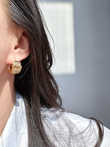 Detailed view of wide gold-plated wave earrings with pavé zircons on a female model