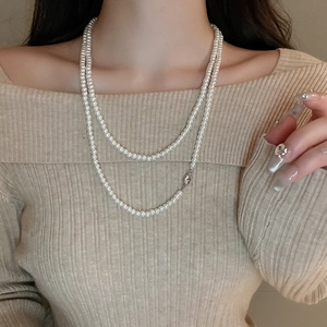Detailansicht der doppellagigen Perlenkette auf einem beigen Pullover mit Textur und Glanz