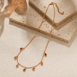 Close-up of gold chain with multi-colored teardrop zircon pendants on stone