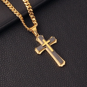 Macro detail of a double-layered gold and dark grey cross pendant on a black leather texture