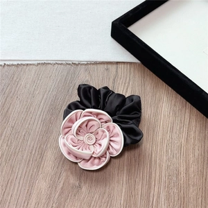 Detail of pink satin camellia flower hair tie with white piping on wood background
