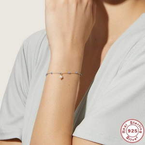 Detail of 925 sterling silver gold bracelet with blue beads and white pearl on wrist
