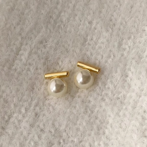 Detailansicht eleganter Perlenohrstecker mit goldenen Metallstäben auf weichem Stoff