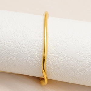 Vista macro di un bracciale aperto dorato a forma di onda con finitura a specchio lucida