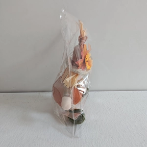 Detail of harvest scarecrow plush doll with sunflower hat in clear protective packaging