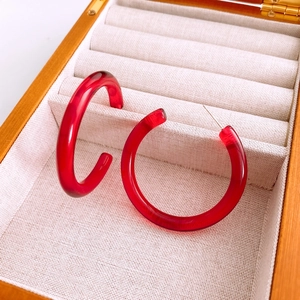 Close-up of red translucent resin C-shape hoop earrings inside a wooden jewelry box