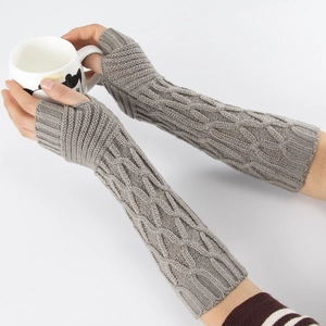 Close-up of grey cable-knit arm warmers with thumb holes worn while holding a mug