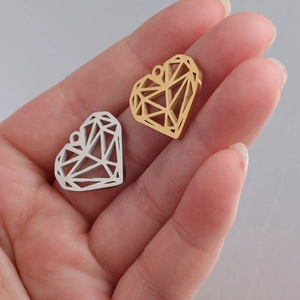 Detailed view of hollow heart pendants in gold and silver finish held in hand