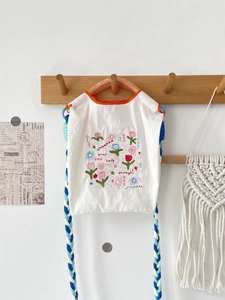 Détail de la broderie florale et de la sangle tissée sur un mini sac en tissu Oxford