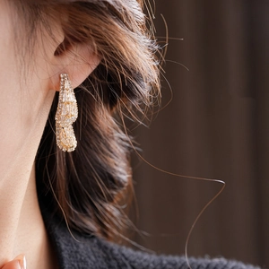 Close-up of elegant gold teardrop earrings with sparkling zircons worn by a model