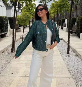 Outdoor shot of a textured dark green sequin jacket styled with wide-leg white trousers