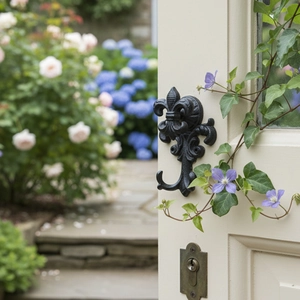 Vintage black cast iron fleur-de-lis wall hook mounted on a white wooden garden door
