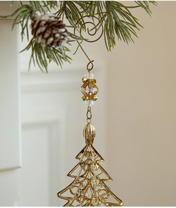Golden iron Christmas tree ornament with elegant beads hanging on a pine branch