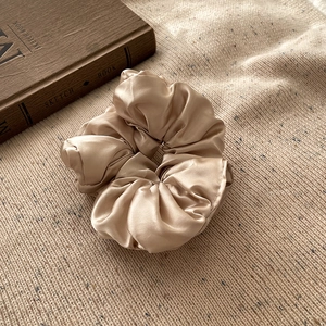 Gros plan du chouchou en satin champagne avec plis doux sur fond en tricot douillet