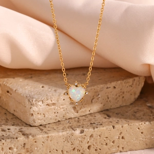Detail of a gold heart necklace featuring a white opal stone set on a stone background