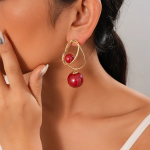 Close-up of gold irregular ring earrings featuring deep red beads worn by a model
