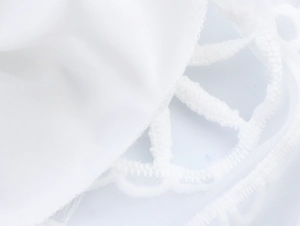 Détail du tissu en maille blanche avec broderie délicate et bordure en dentelle florale